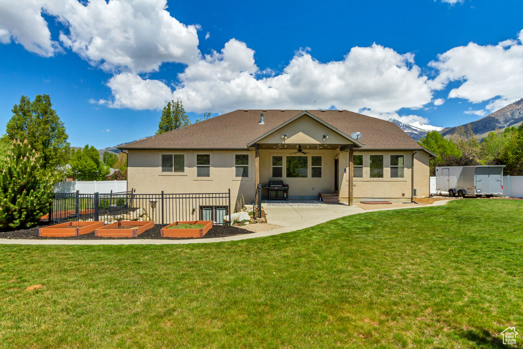 Rear view of property with stucco siding, ceiling fan, a patio area, a vegetable garden, and a mountain view
