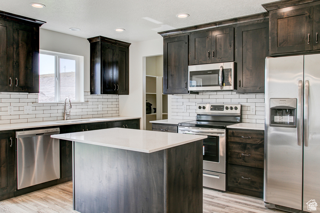 Kitchen with appliances with stainless steel finishes, a sink, decorative backsplash, light wood-type flooring, and recessed lighting