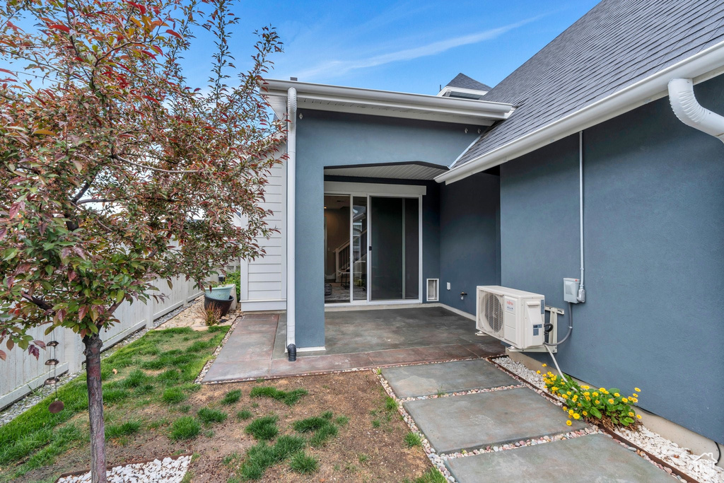 Entrance to property featuring a cooling unit, a shingled roof, a patio, fence, and stucco siding