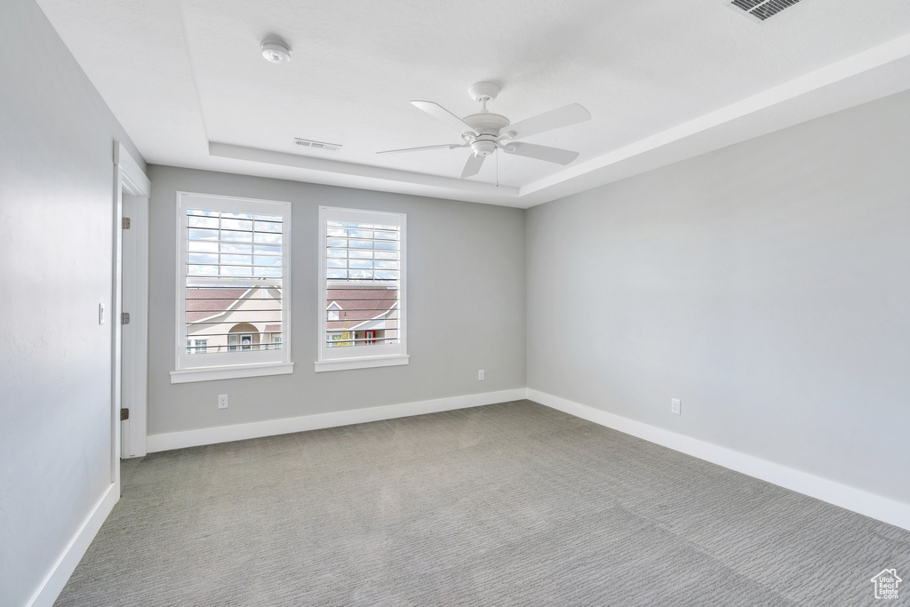 Spare room with carpet, ceiling fan, baseboards, a smoke detector, and a tray ceiling