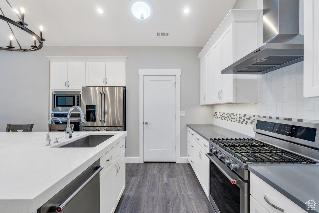 Kitchen with appliances with stainless steel finishes, wall chimney exhaust hood, a sink, backsplash, and dark wood finished floors