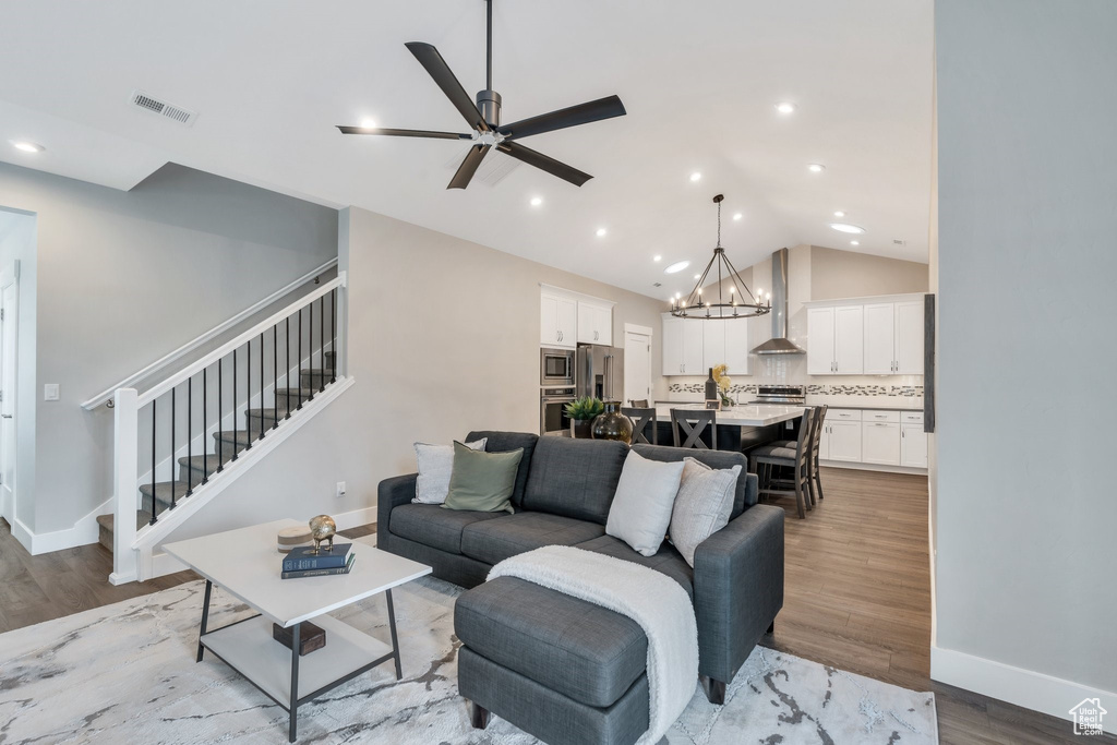 Living area featuring stairs, a chandelier, a ceiling fan, light wood-type flooring, and baseboards