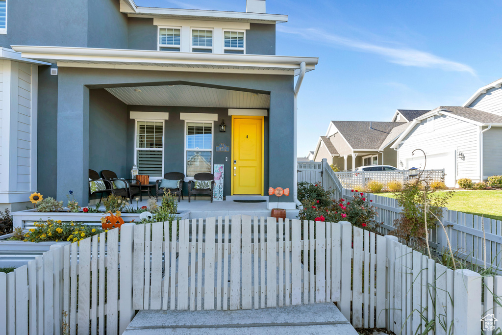 View of front of property with a porch, stucco siding, a fenced front yard, and an attached garage