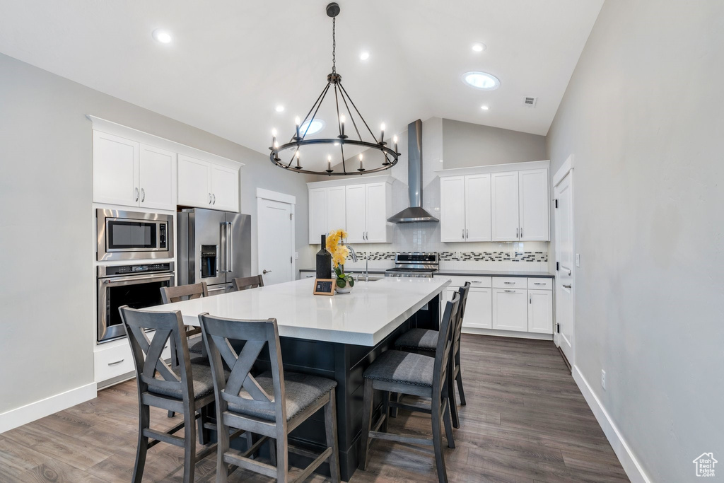 Kitchen with stainless steel appliances, wall chimney exhaust hood, a chandelier, backsplash, and vaulted ceiling