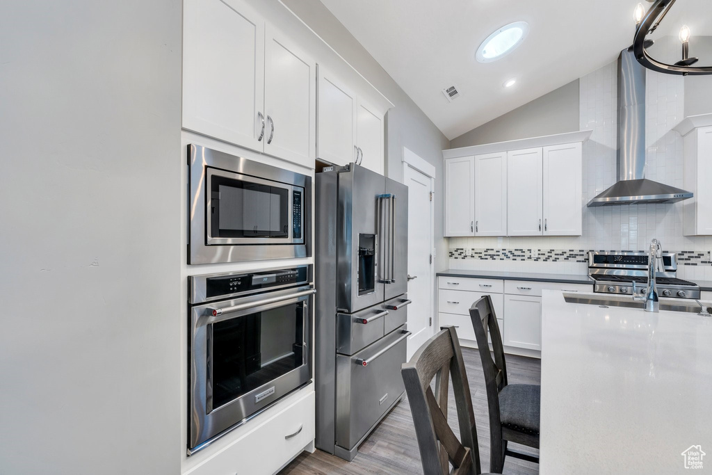 Kitchen with stainless steel appliances, vaulted ceiling, wood finished floors, backsplash, and white cabinets