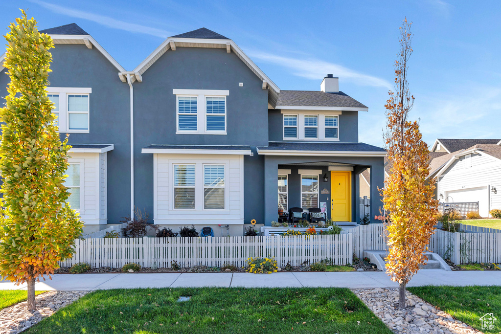 Traditional home with stucco siding, covered porch, a fenced front yard, and a chimney