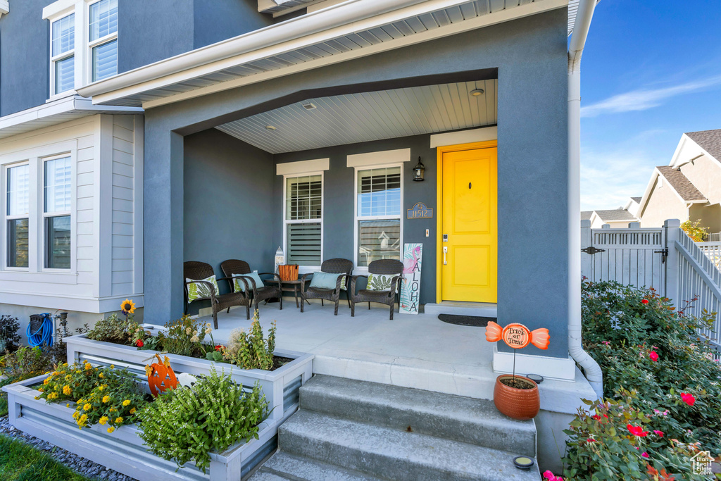 Entrance to property featuring covered porch, stucco siding, and fence