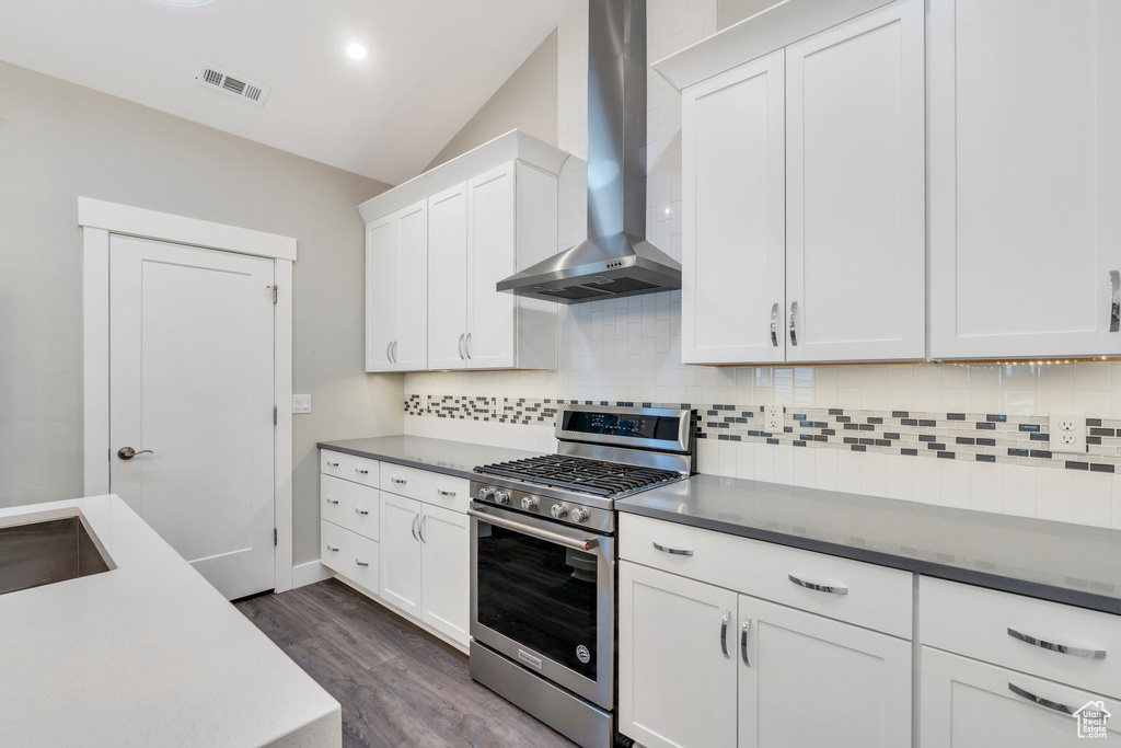 Kitchen with gas stove, wall chimney range hood, backsplash, dark wood-type flooring, and white cabinetry
