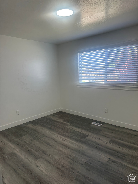 Empty room featuring baseboards and dark wood-type flooring