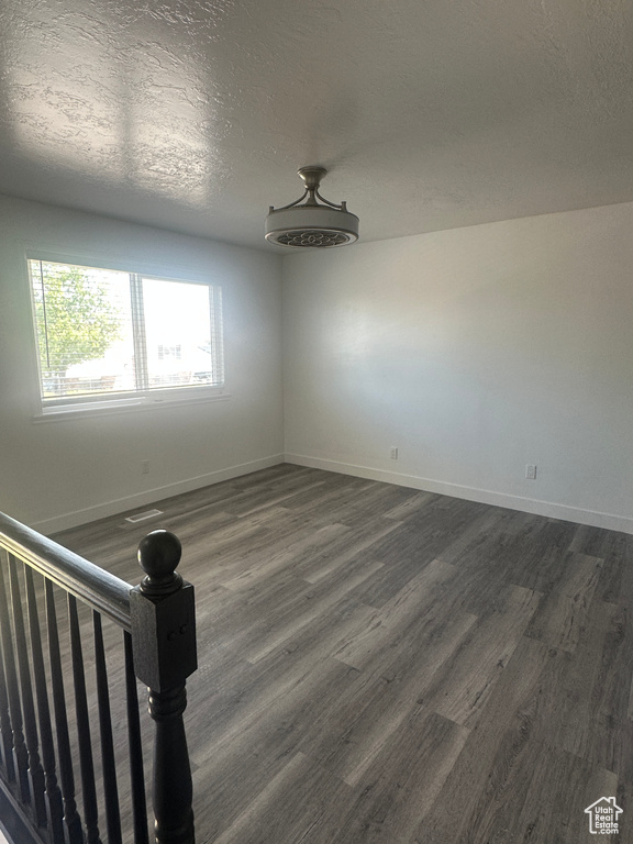 Spare room featuring dark wood-type flooring, baseboards, and a textured ceiling