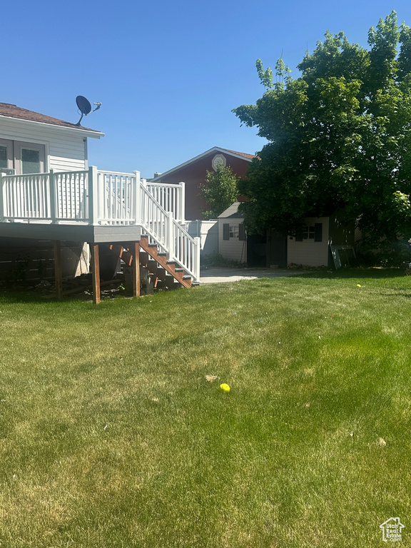 View of green lawn featuring a wooden deck and stairway