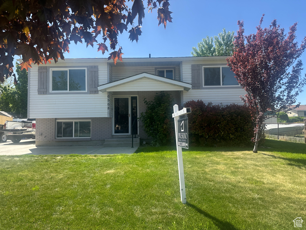 Split level home featuring a front yard, brick siding, and a patio area
