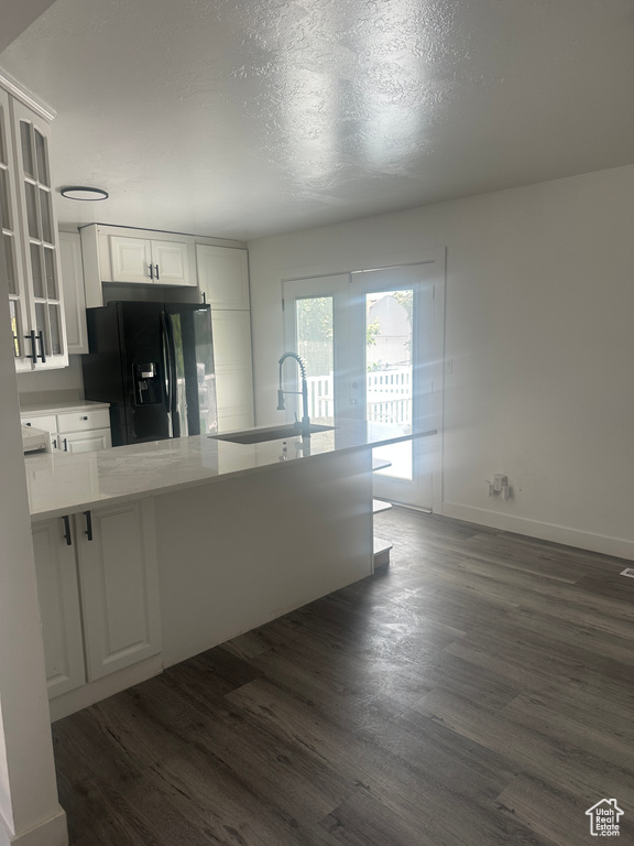 Kitchen featuring black fridge with ice dispenser, a sink, dark wood-type flooring, glass insert cabinets, and white cabinetry