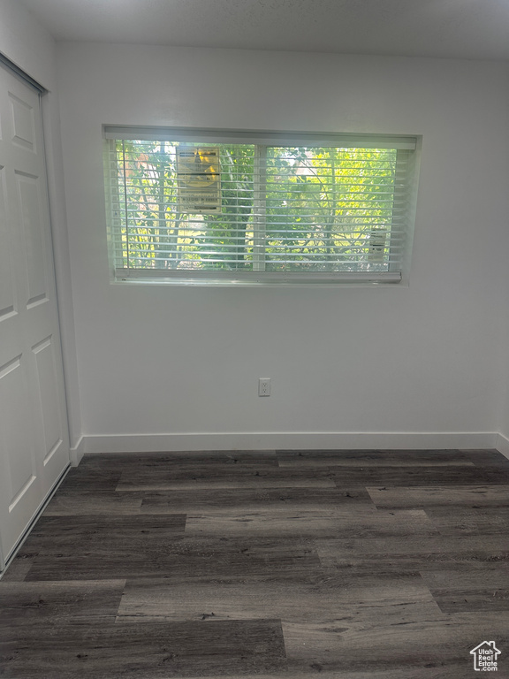 Empty room featuring healthy amount of natural light, baseboards, and dark wood-type flooring