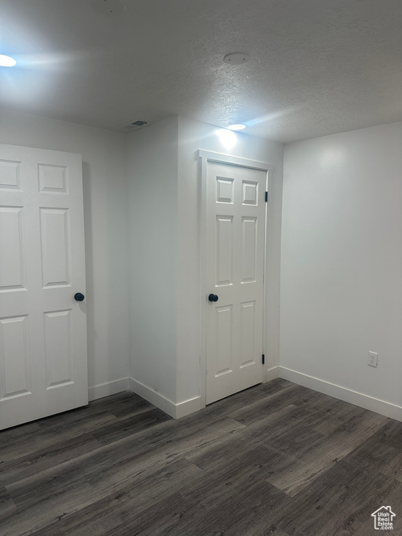 Empty room featuring dark wood-type flooring, baseboards, and a textured ceiling
