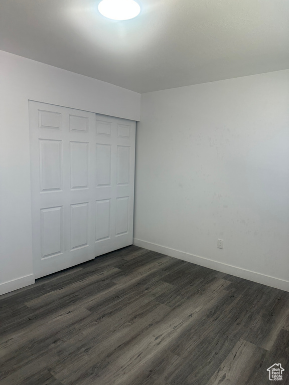 Unfurnished bedroom featuring dark wood-style flooring, baseboards, and a closet