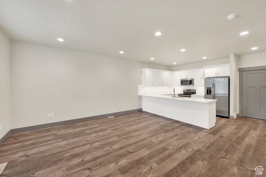 Kitchen with stainless steel appliances, a peninsula, wood finished floors, baseboards, and recessed lighting
