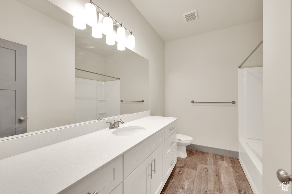 Bathroom featuring wood finished floors, vanity, toilet, bathing tub / shower combination, and baseboards