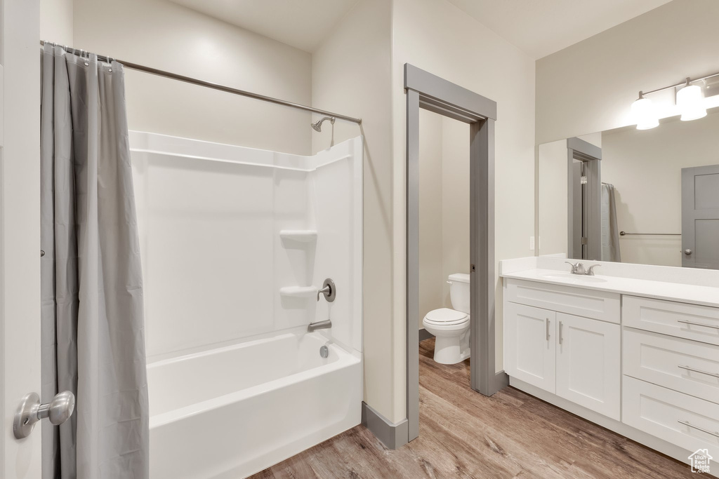 Bathroom featuring wood finished floors, toilet, vanity, shower / tub combo, and baseboards