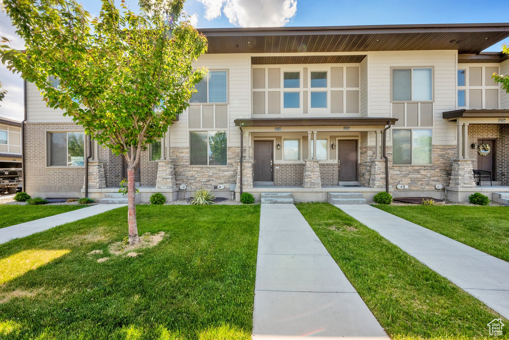 View of front of home with a front yard, covered porch, and stone siding