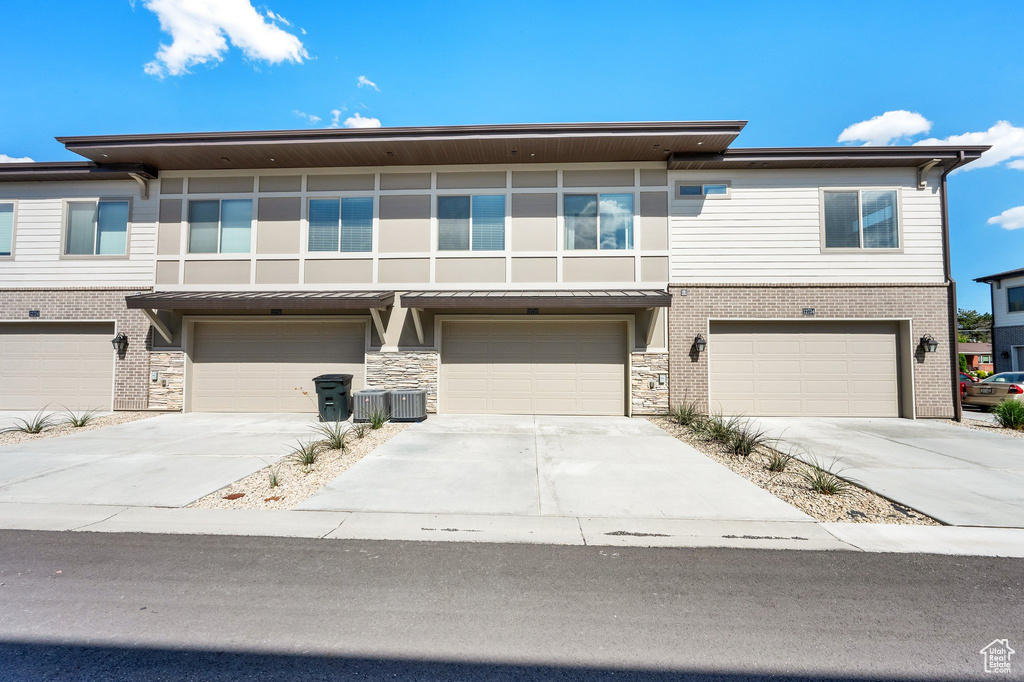 View of front of property with an attached garage, driveway, central AC, and brick siding