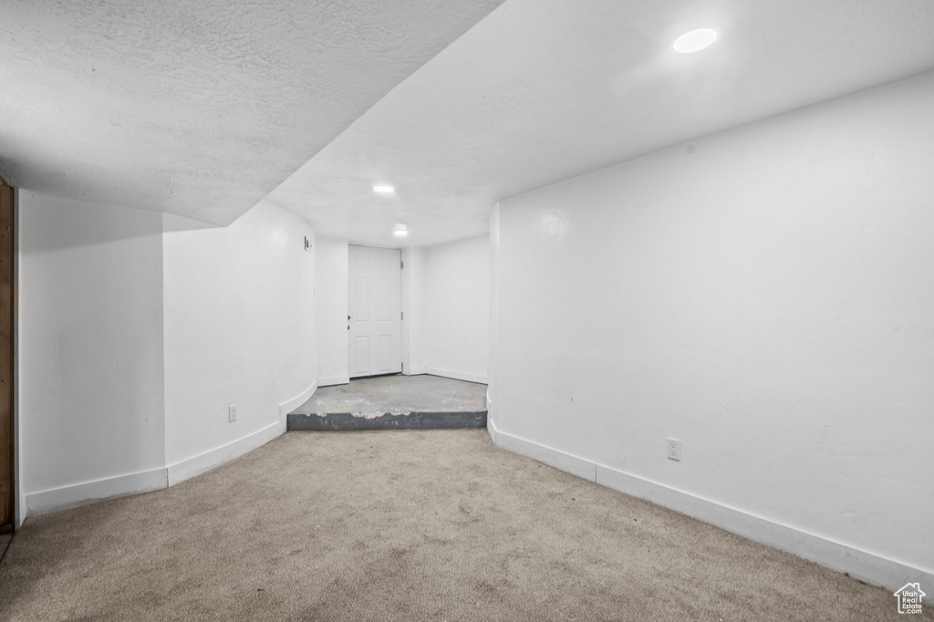 Finished below grade area featuring baseboards, carpet flooring, and a textured ceiling