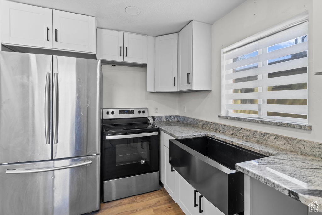 Kitchen featuring appliances with stainless steel finishes, light stone counters, and white cabinetry