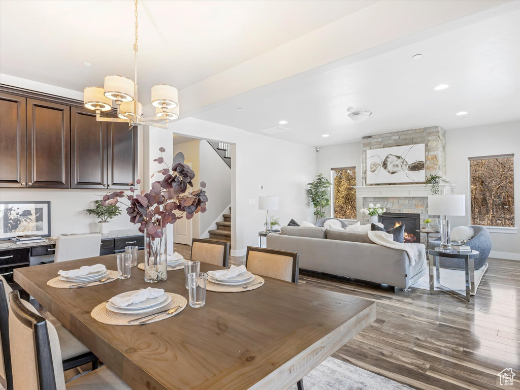 Dining space featuring stairs, wood finished floors, a chandelier, recessed lighting, and a stone fireplace