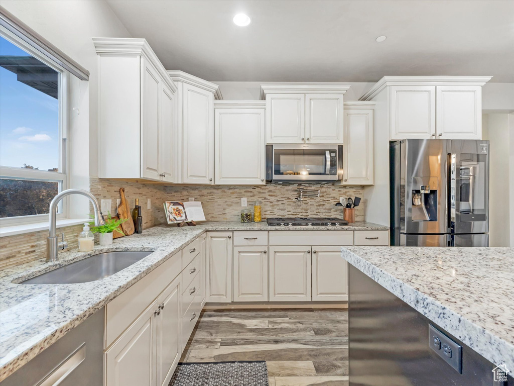 Kitchen with stainless steel appliances, a sink, light wood-style flooring, backsplash, and white cabinets