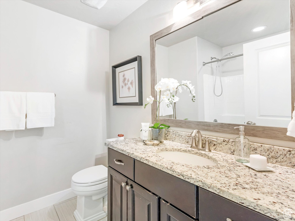 Full bathroom with toilet, a shower, baseboards, and vanity