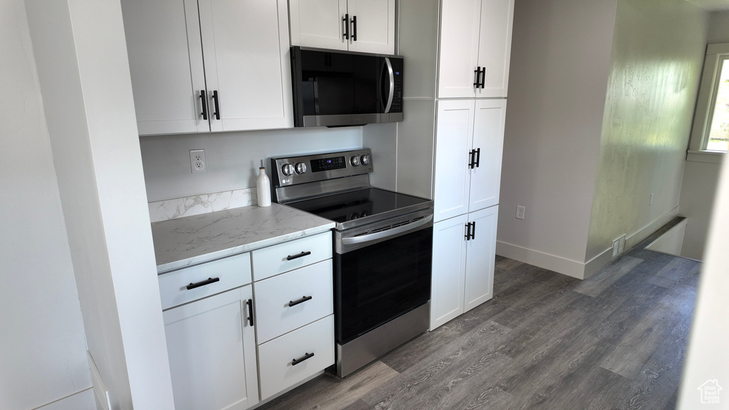 Kitchen with stainless steel electric range oven, wood finished floors, light stone counters, white cabinetry, and baseboards