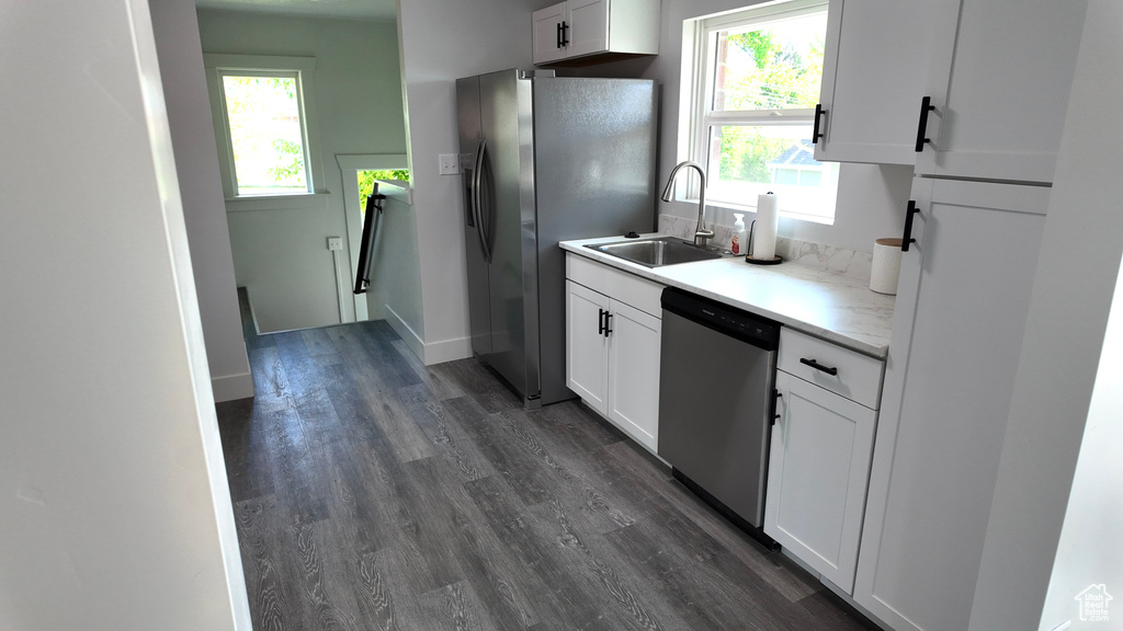 Kitchen with appliances with stainless steel finishes, a sink, dark wood-style floors, and white cabinetry