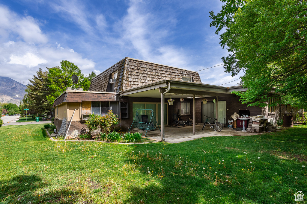 Rear view of house featuring a patio, mansard roof, a lawn, brick siding, and a mountain view