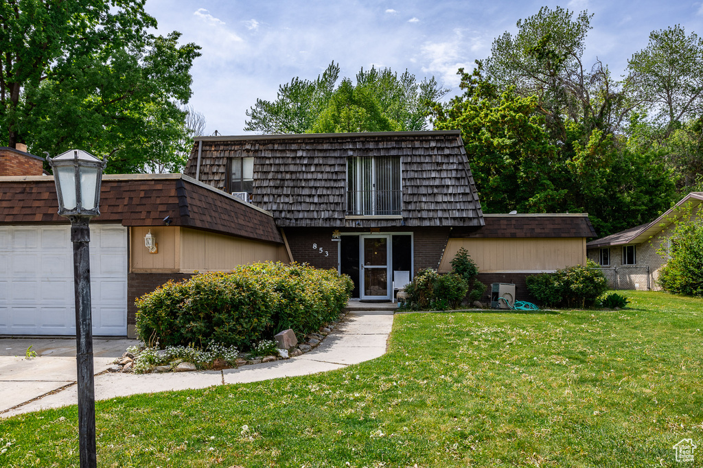 View of property with mansard roof, brick siding, a front lawn, an attached garage, and concrete driveway