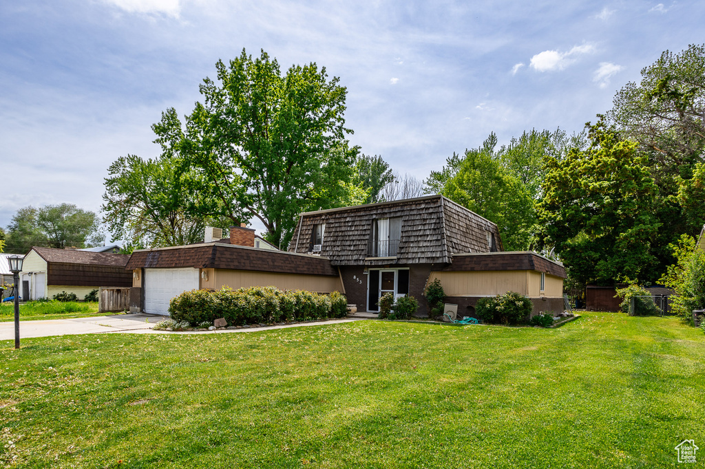 Mid-century modern home with mansard roof, concrete driveway, and a front yard
