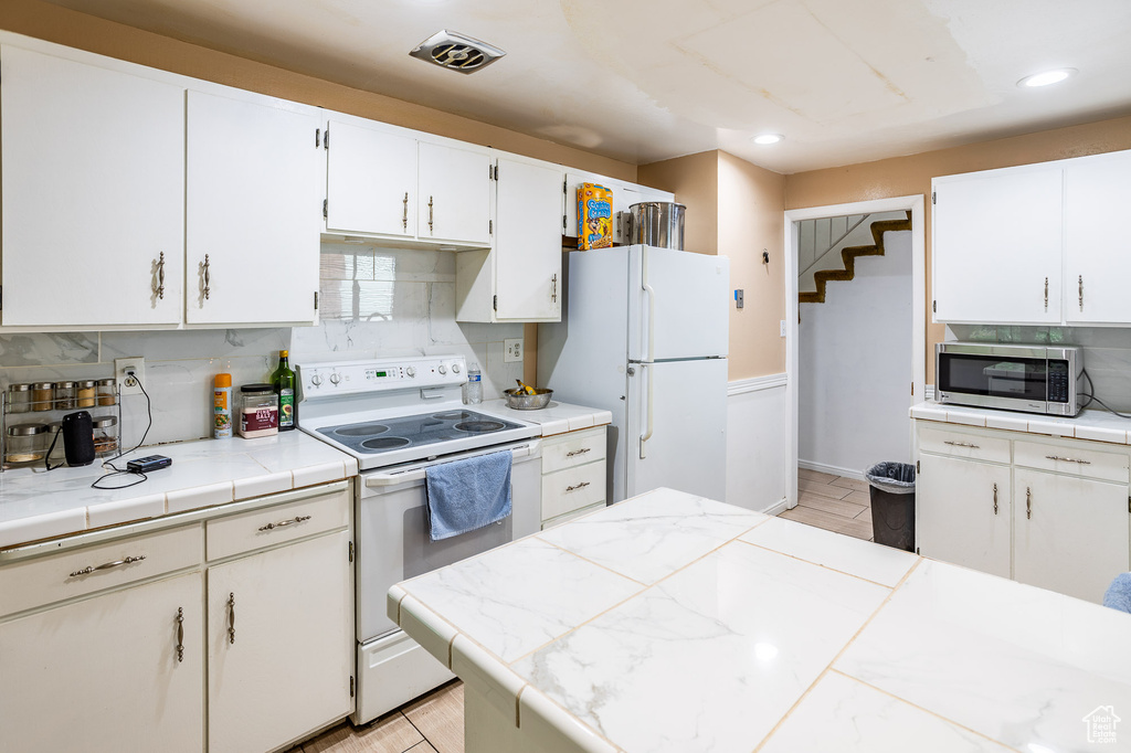 Kitchen featuring white appliances, recessed lighting, decorative backsplash, white cabinetry, and tile countertops