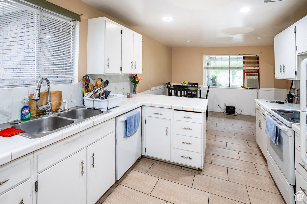 Kitchen featuring white appliances, a peninsula, a sink, white cabinetry, and tile counters