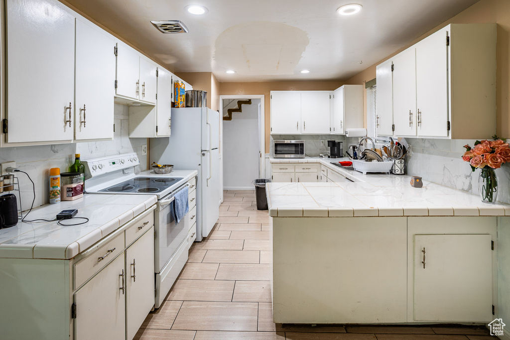 Kitchen with white appliances, tasteful backsplash, recessed lighting, tile counters, and a peninsula