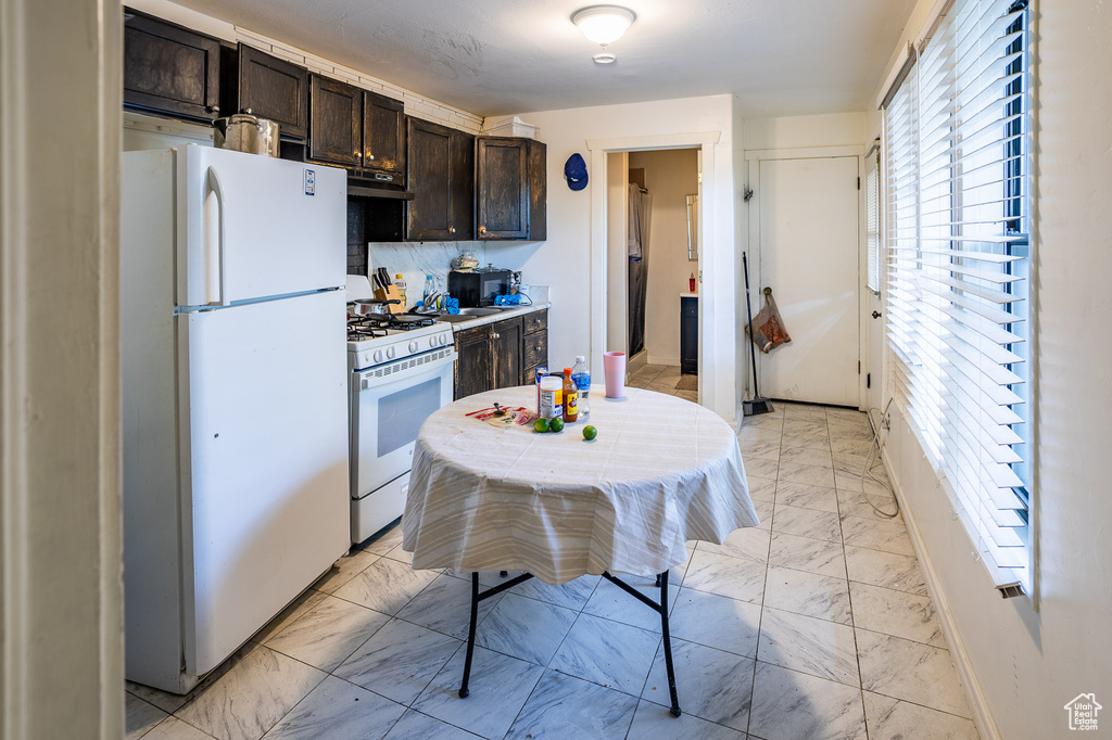 Kitchen with white appliances, light marble finish flooring, dark brown cabinets, under cabinet range hood, and light countertops