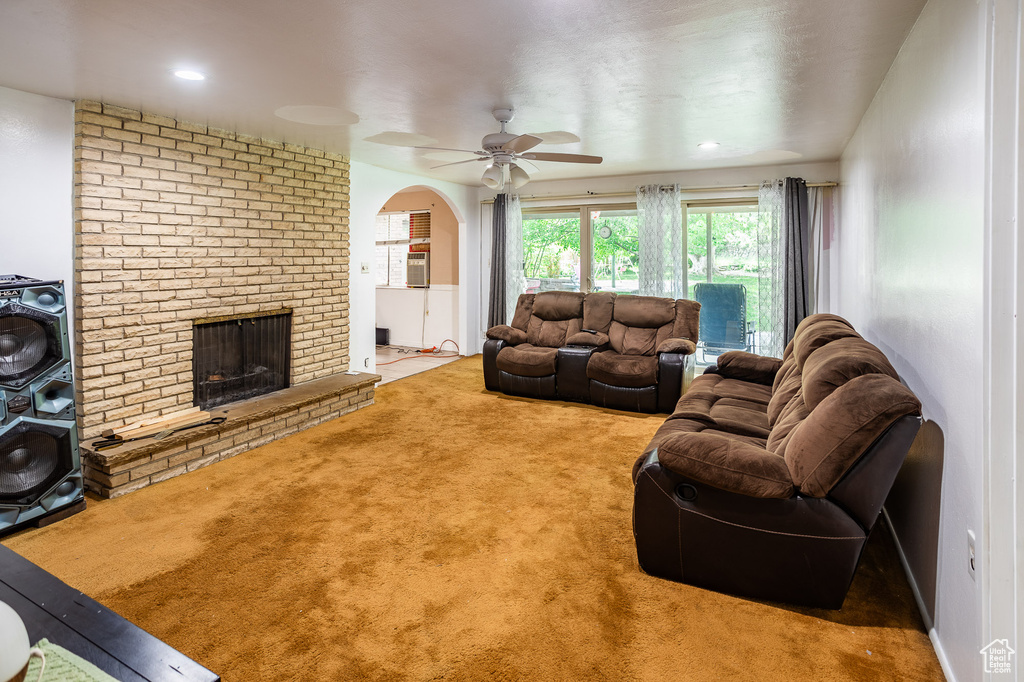 Living area with carpet floors, a ceiling fan, a fireplace, and arched walkways