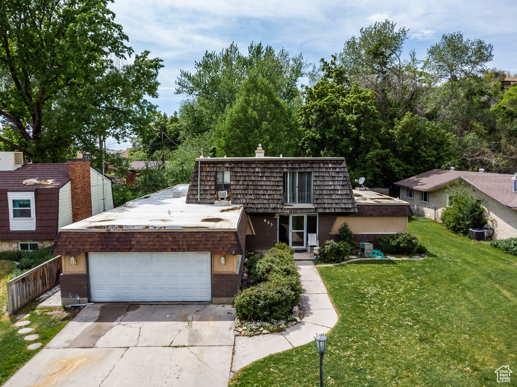 View of front of property with brick siding, driveway, an attached garage, mansard roof, and a chimney