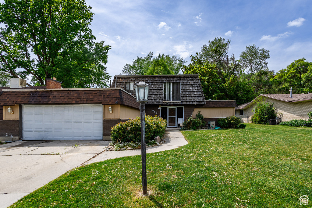 View of front property featuring mansard roof, brick siding, a front lawn, concrete driveway, and a garage