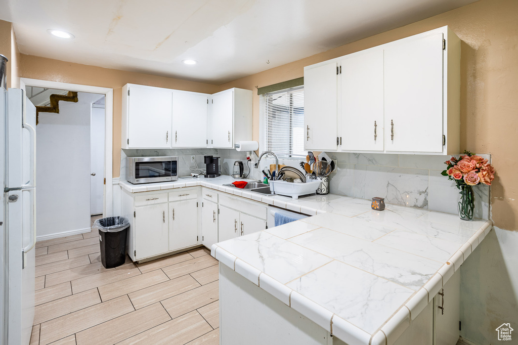 Kitchen with stainless steel microwave, backsplash, a sink, freestanding refrigerator, and white cabinets