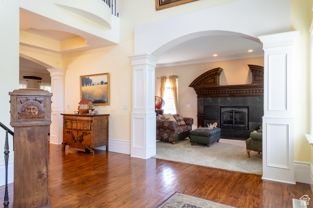 Foyer with wood finished floors, a fireplace, arched walkways, ornate columns, and ornamental molding