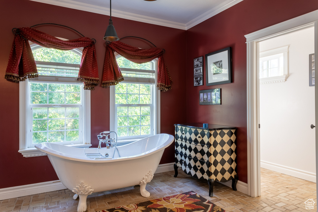 Bathroom featuring baseboards, plenty of natural light, a freestanding bath, brick patterned flooring, and crown molding