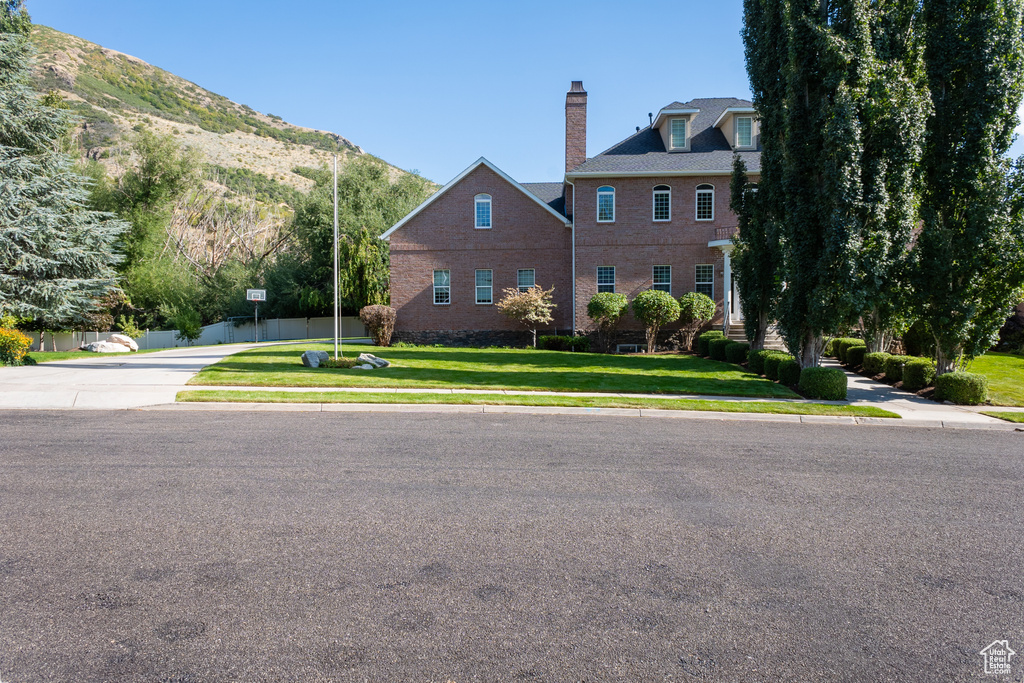 View of front facade featuring a chimney, a mountain view, a front yard, and brick siding