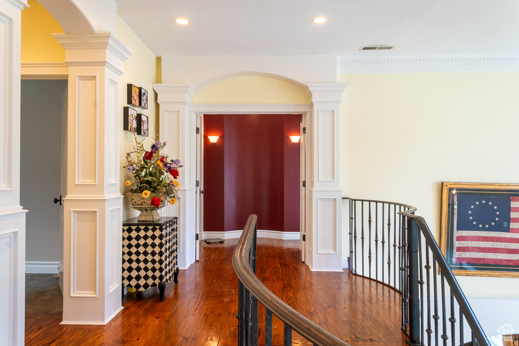 Hall with ornate columns, dark wood finished floors, an upstairs landing, recessed lighting, and arched walkways
