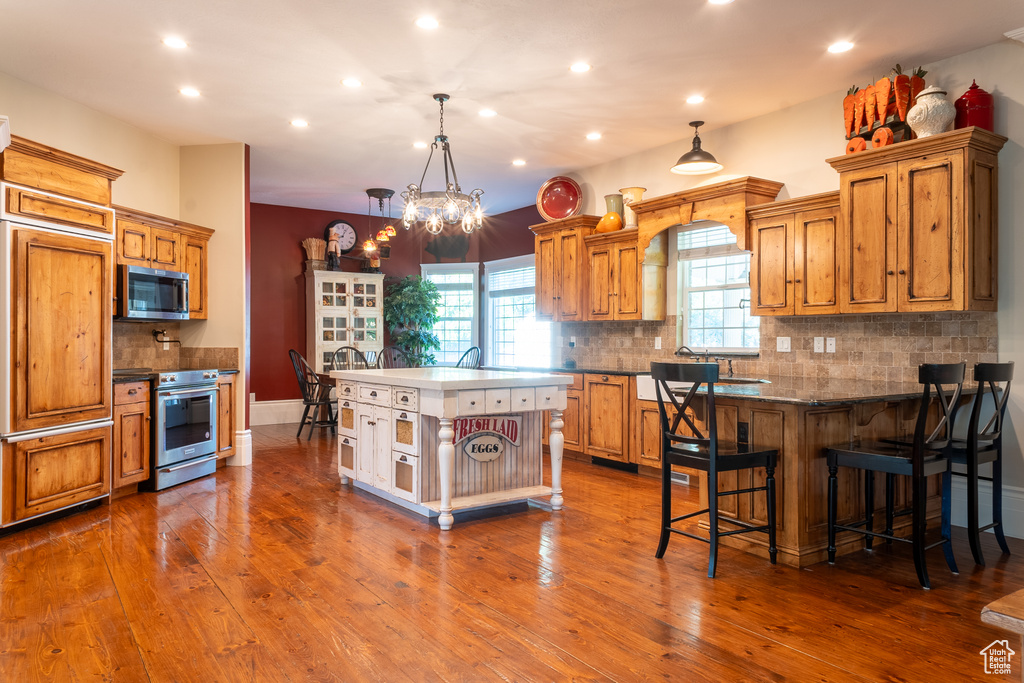 Kitchen featuring appliances with stainless steel finishes, tasteful backsplash, recessed lighting, brown cabinets, and a breakfast bar