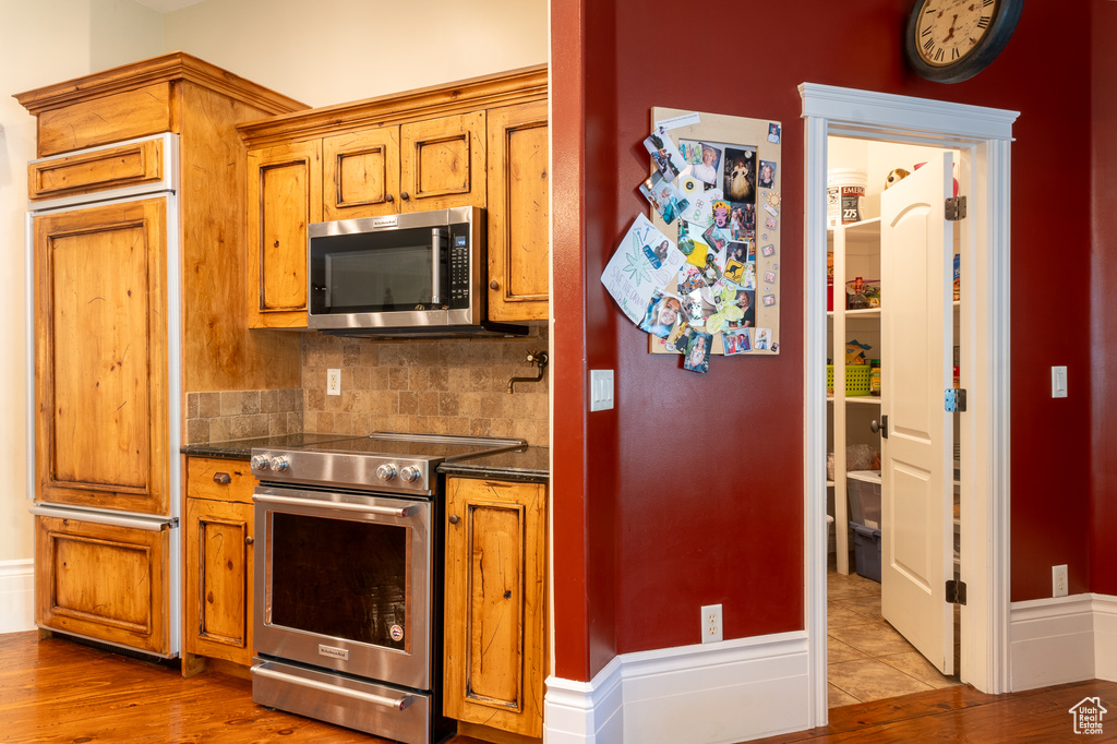 Kitchen featuring stainless steel appliances, dark countertops, brown cabinets, decorative backsplash, and light wood finished floors