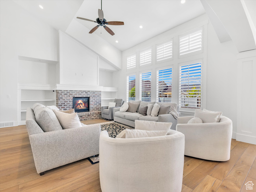 Living room featuring a towering ceiling, light wood-type flooring, built in shelves, a ceiling fan, and recessed lighting